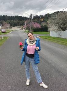 woman colourfully dressed holding flowers and moss standing in suburban street with spring blossom on trees